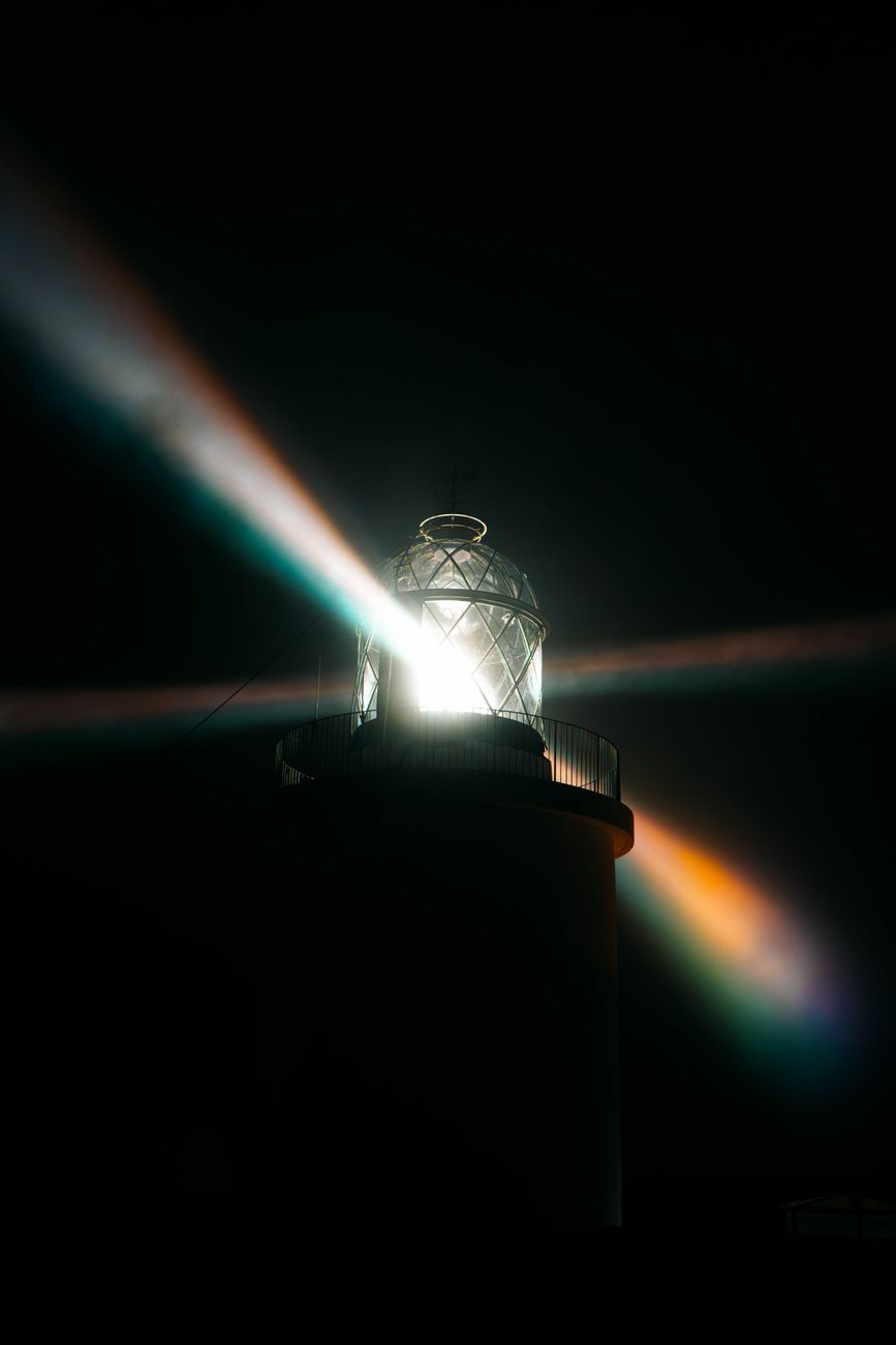 A lighthouse casting vibrant light beams at night, creating a dramatic effect.